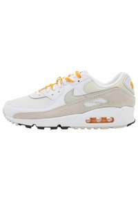 Baskets Nike Air Max 90 avec tige en cuir blanc, accents en daim beige, lacets orange et unité d'air visible dans la semelle.