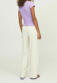 Lila ribbad kortärmad tröja kombinerad med krämfärgade vida byxor. Outfiten har en figurnära topp och lösa byxor, vilket skapar en kontrast i former.