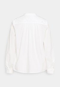 Biała bluzka z długim rękawem, z guzikami na mankietach, marszczonym materiałem poniżej karczka oraz okrągłym kołnierzykiem, widoczna z tyłu.