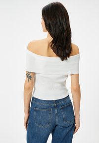 Weißes, schulterfreies, geripptes Oberteil mit passformbetontem Design, kombiniert mit blauen, hoch taillierten Jeans mit Gesäßtaschen und klassischer Denim-Textur.