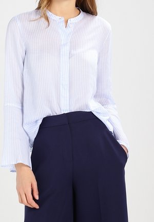 Femme portant un chemisier à manches longues rayé bleu clair, rentré dans un pantalon large taille haute bleu marine foncé.