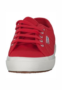 Scarpa da ginnastica rossa in tela con suola in gomma bianca, dotata di lacci piatti e occhielli metallici. La tomaia ha una finitura testurizzata e un dettaglio logo laterale.