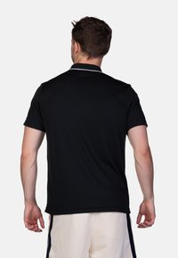 Polo nero con colletto bianco a contrasto, maniche corte e texture liscia, mostrato da dietro con dettagli minimi.