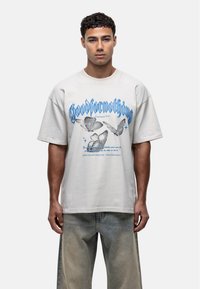 Lichtgrijze oversized T-shirt met blauwe vlinderafbeeldingen en de tekst "Goodfornothing", gemaakt van katoen met een zachte textuur.