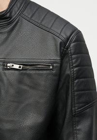 Black leather jacket with textured grain, quilted shoulder panels, and a horizontal zippered chest pocket.