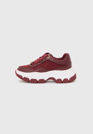 Sneaker bordeaux con suola bianca spessa, battistrada strutturato e lacci, posizionato su uno sfondo grigio chiaro uniforme.