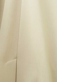 Tessuto beige chiaro, dalla superficie liscia, caratterizzato da una leggera lucentezza e un taglio pulito con un dettaglio a cucitura laterale. Adatto per capi su misura.