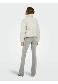 Chaqueta acolchada de color gris claro con cuello alto, diseño corto, puños acanalados y combinada con vaqueros acampanados de color gris claro.