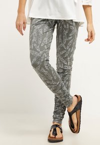 Šedé legíny s bílým vzorem peří, s úzkým střihem a nařasenými detaily. V kombinaci s hnědými a černými žabkami.