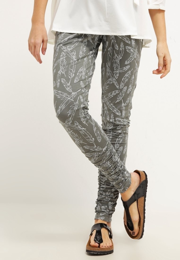 Šedé legíny s bílým vzorem peří, s úzkým střihem a nařasenými detaily. V kombinaci s hnědými a černými žabkami.