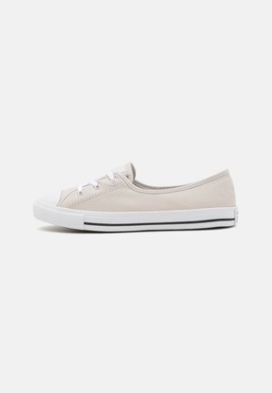 Lage beige canvas sneaker met witte rubberen zool, witte veters en een zwarte streep langs de zoolrand, getoond in zijaanzicht.