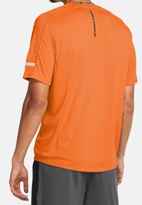 Camiseta atlética naranja con cuello redondo, mangas cortas, acentos texturizados en los hombros y un logo negro en la parte posterior. Fabricada con tela ligera.