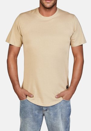 Beige Kurzarm-T-Shirt aus weichem Stoff, mit Rundhalsausschnitt und geradem Saum, kombiniert mit hellblauen Jeans.