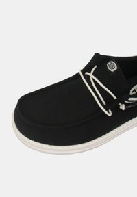 Scarpa nera slip-on con tomaia in tela, suola in gomma bianca e lacci bianchi a contrasto. Presenta un logo sul lato e dettagli cuciti.