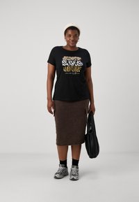 Juoda marškinėliai su grafine gyvūnų spauda auksine ir balta spalvomis, derinami su rudais džinsiniais sijonais, pilkais sportinėmis bateliais ir juoda petneša.