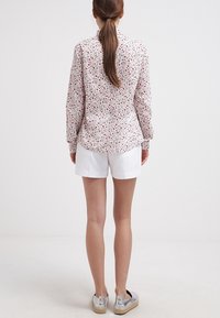 Vit blommig långärmad skjorta med rosa och gröna mönster, ihop med texturerade vita shorts och silverfärgade skor. Synlig bakvy.