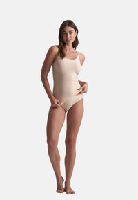 Costume da bagno intero color carne con scollatura quadrata e spalline sottili, caratterizzato da una texture liscia e elastica e design senza cuciture, ideale per nuotare.