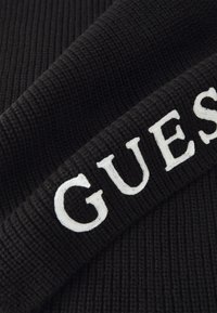 Juodas įribiotas audinys su baltu siuvinėtu tekstu "GUESS." Medžiaga turi tekstūruotą apdailą, pasižyminčią kasdienišku dizainu.