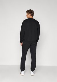 Sweatshirt de algodão preto e calças de jogger coordenadas com um corte descontraído. O conjunto apresenta punhos canelados e um decote redondo, combinado com ténis brancos.