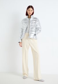 Giubbotto a sacco argento con design trapuntato, colletto alto e zip frontale. Abbinato a pantaloni beige a vita alta e scarpe grigie. Stile minimalista.