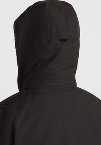 Čierna kapucňová bunda s textúrovanou, vodeodolnou látkou. Má hladký povrch a švy, ktoré zdôrazňujú minimalistický dizajn.