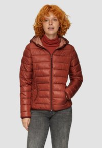 Puchowa kurtka w kolorze rdzy z kapturem, z pikowanymi panelami, przednim zamkiem i bocznymi kieszeniami. Noszona na bordowym golfie.