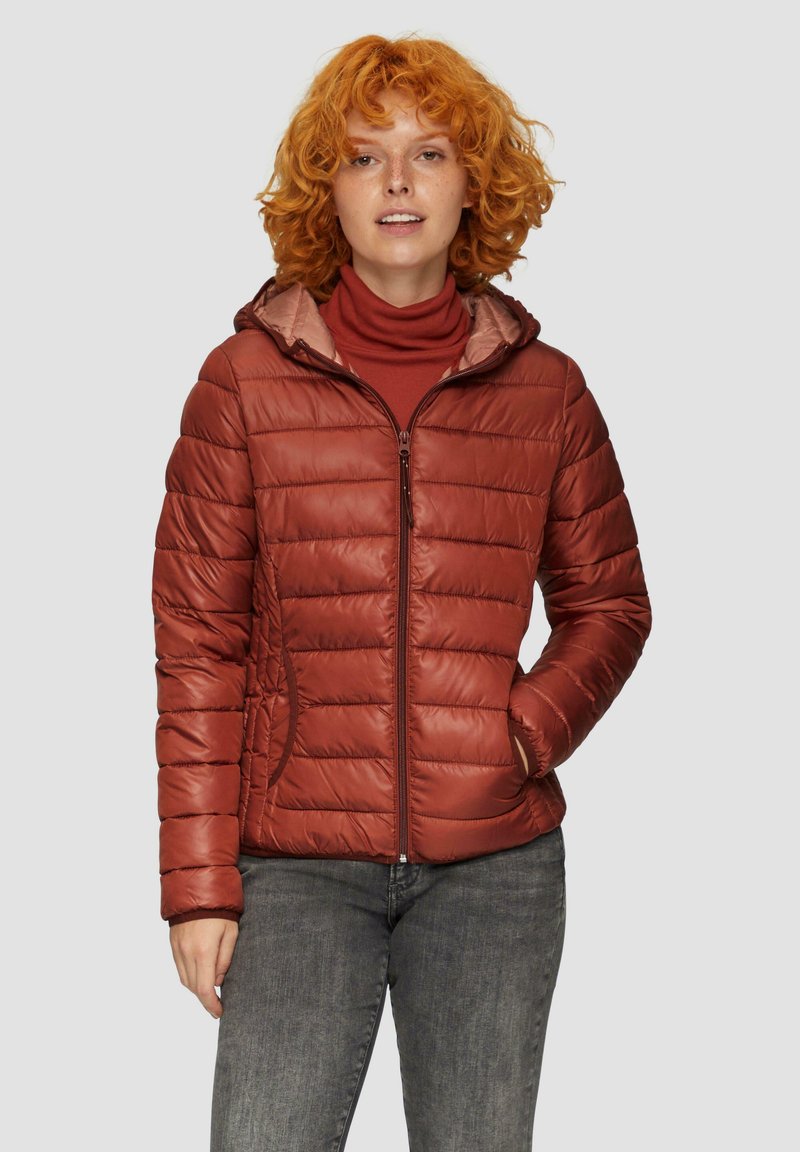 Puchowa kurtka w kolorze rdzy z kapturem, z pikowanymi panelami, przednim zamkiem i bocznymi kieszeniami. Noszona na bordowym golfie.