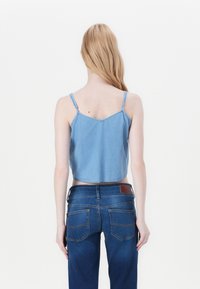Top in denim tagliato con spalline sottili, lavaggio azzurro chiaro, bordi sfrangiati, abbinato a jeans blu scuro caratterizzati da un sottile motivo di cucitura.