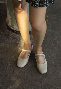 Zapatos Mary Jane en color beige con punta redondeada y suela plana, que cuentan con una sola correa en la parte superior. Textura de cuero suave, diseño minimalista.