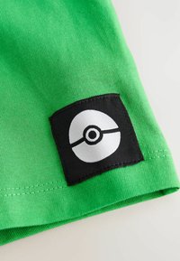 Roheline puuvillakangas, millel on must paik valge Poké Ball'i kujundusega. Paik on õmmeldud kanga äärde.