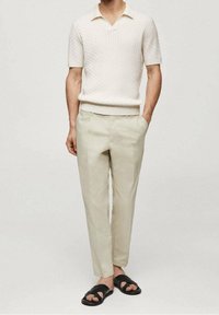 Krémový svetr s krátkými rukávy a texturovaným vzorem pletení, doplněný světle béžovými kalhotami a černými sandály na plochém podpatku. Jednoduchý, moderní design.