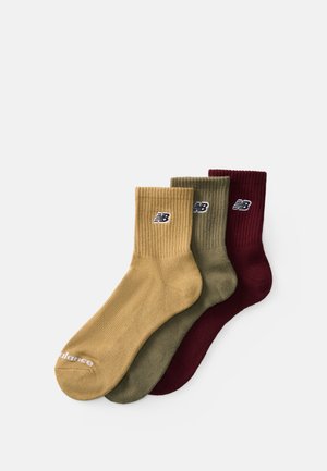 Three pairs of ribbed socks in olive green, mustard yellow, and burgundy, featuring a small logo on the cuff and soft texture.