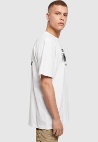 White cotton t-shirt with short sleeves, featuring a black graphic design on the front and back. Relaxed fit and round neckline.