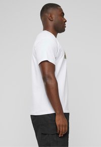 Hvid kortærmet t-shirt med grafisk design på brystet, båret med sorte cargo shorts. Glat tekstur, afslappet pasform.