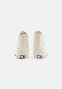 Bílé vysoké plátěné tenisky se zaobleným špičkou a květinovými výšivkami v růžové, modré a oranžové barvě. Černé logo "Converse All Star" na patě.