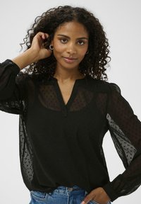 Zwarte blouse van doorschijnende, gestructureerde stof, met een V-hals en lange, opgeblazen mouwen. Inclusief knoopdetails op de mouwen.