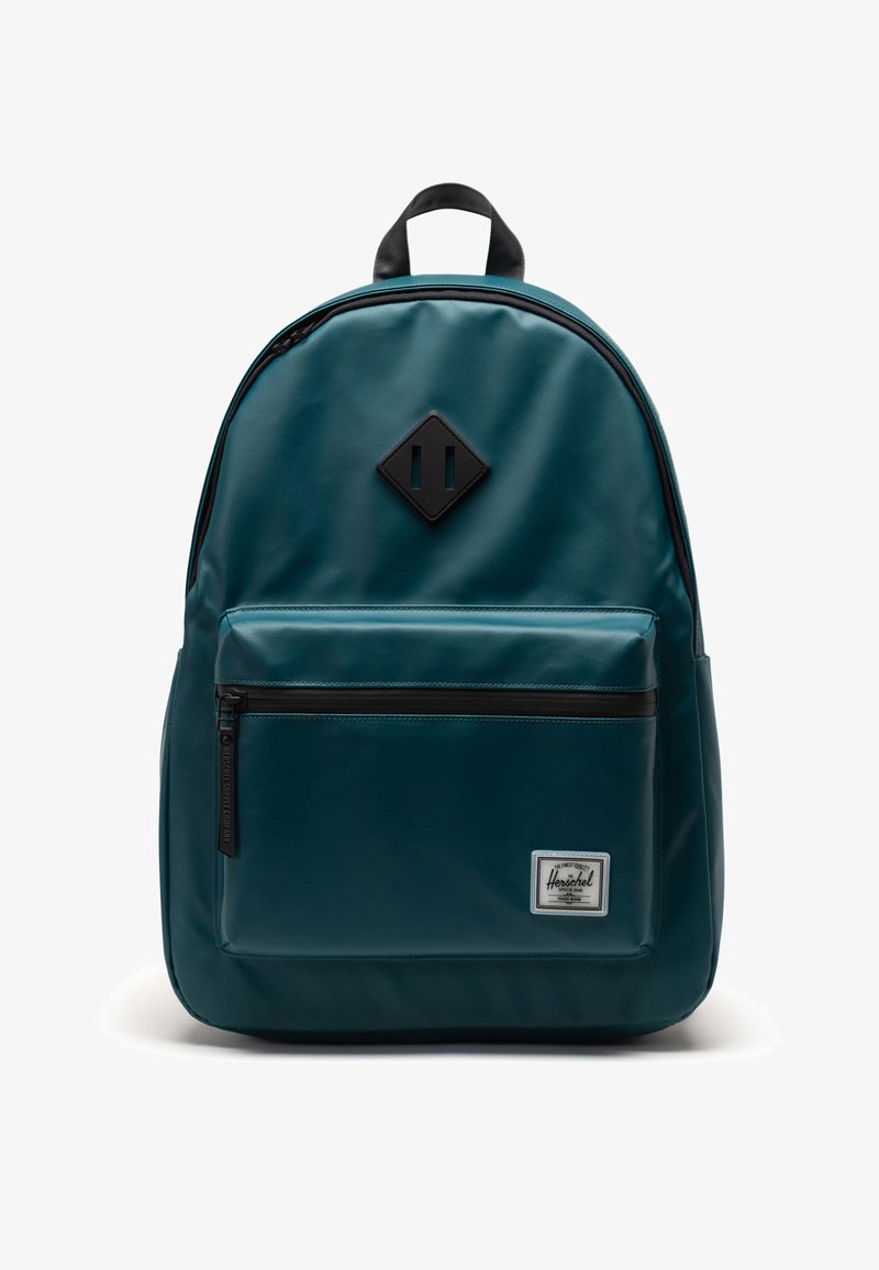 Teal ryggsäck med en slät yta, svarta dragkedjeaccsenter och en diamantlogotyp på lapparna. Har en framficka och vadderad baksida.