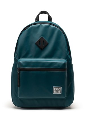 Sac à dos teal avec une texture lisse, des accents de fermeture éclair noirs et un patch logo en forme de diamant. Il dispose d'une poche frontale et d'un dos rembourré.