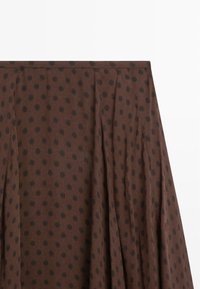 Brown skirt with a textured fabric featuring black polka dots, pleated design, and a wide waistband.