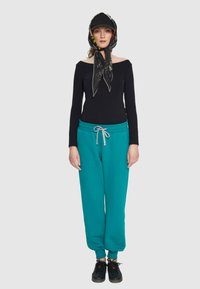 Czarny top bez ramiączek, tealowe dresy ze sznurkiem, wzorzysty szalik i czarna czapka, czarne sneakersy, casualowy styl.