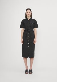 Rochie midi neagră, cu mâneci scurte, croială cu nasturi în față, două buzunare la piept, talie cu cordon și nasturi aurii. Asortată cu pantofi slip-on negri.