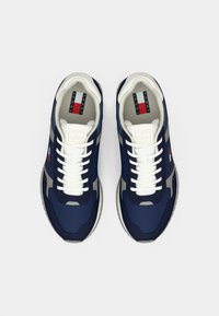 Een paar marineblauwe en witte sneakers van Tommy Jeans met witte veters en een logo patch op de tong en zijkant, bekeken van bovenaf.