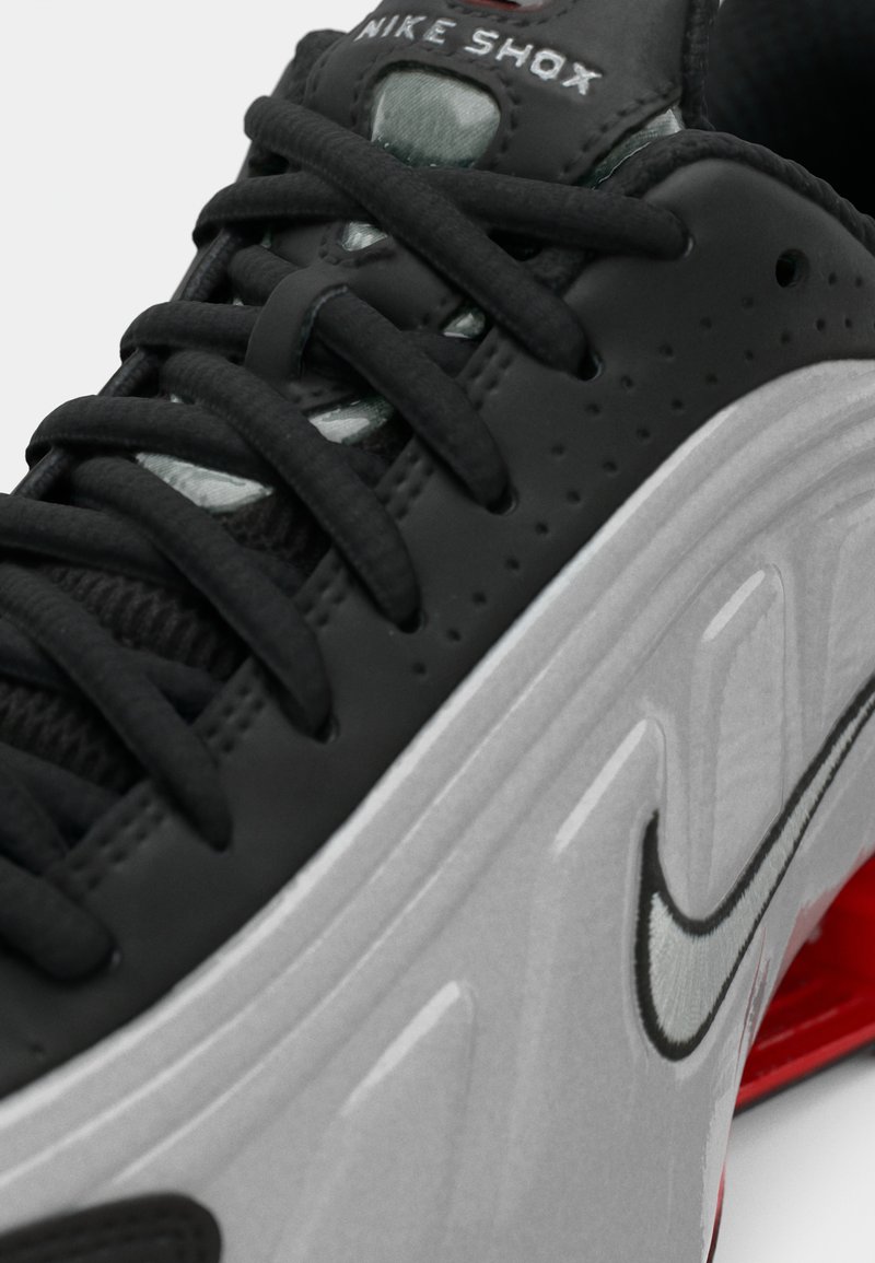 Gros plan sur une sneaker Nike Shox noire et grise avec des lacets noirs et un amorti rouge visible dans la semelle.