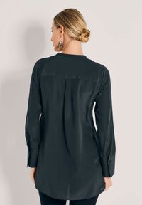 Dunkelseidenbluse mit langen Ärmeln, einem knöpfbaren Bündchen und einer Faltenlegung am Rücken, mit abgerundetem Saum und glatter Textur.