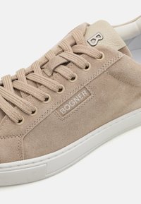 Beige semsket sneaker med teksturert overflate, rund tå, hvit gummisåle og vevde snøringer. Har en logoplass i lys skinn.