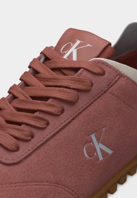 Αθλητικό παπούτσι σουέντ σε σκουριά απόχρωση με κορδόνια στο ίδιο χρώμα, με το λογότυπο "cK" στο πλάι και στη γλώσσα, και καφέ υφασμένη σόλα.