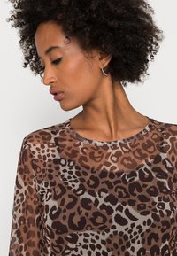 T-shirt transparente castanha com um padrão de estampa de leopardo em diferentes tons de castanho e preto. Decote redondo e mangas longas.