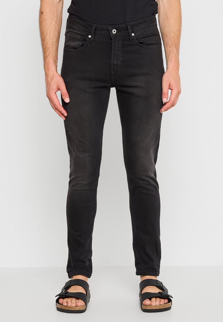 Jeans negros de corte ajustado con una textura suave, cinco bolsillos y cremallera. Llevados con sandalias negras con una tira hebillada.