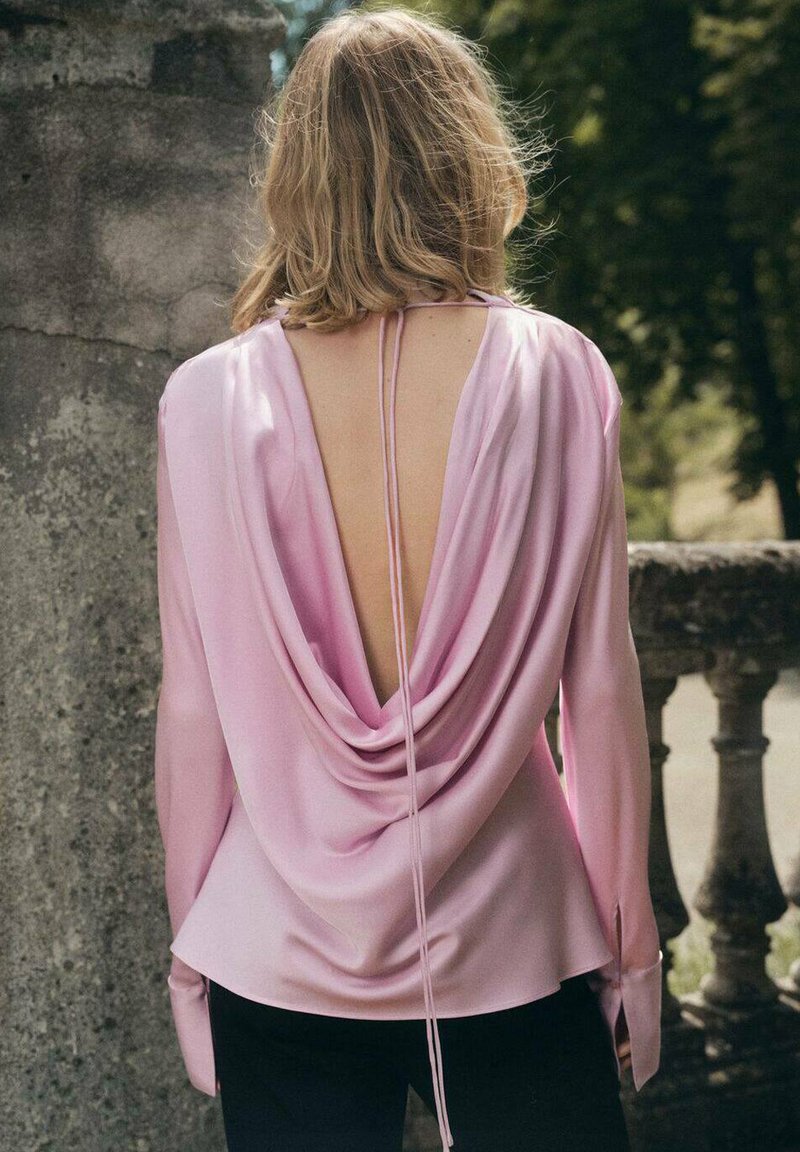 Rosafarbene Satinbluse mit drapiertem Rücken, langen Ärmeln und Bindeschluss. Glatte Textur.