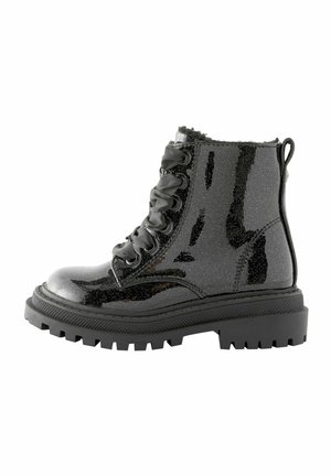 Bottine noire brillante à lacets, semelle épaisse et cramponnée, avec une languette en tissu à l'arrière, conçue pour un usage décontracté ou robuste.